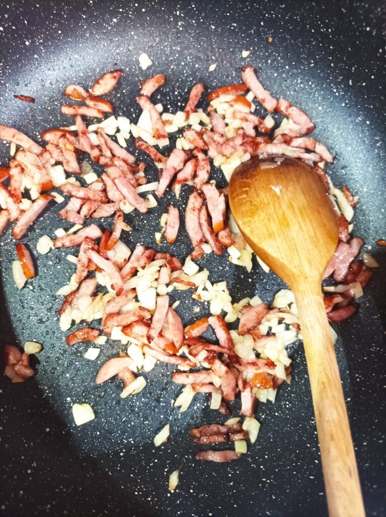 Pokrojony boczek smażony na patelni jako dodatek do zupy z dyni Pokrojony boczek podsmażony na patelni z cebulka jako dodatek do zupy z dyni przepis