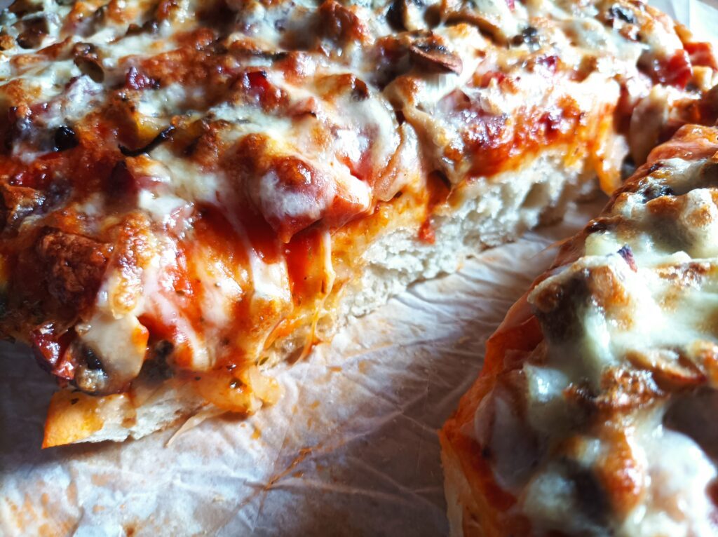 Pizza na grubym cieście z kiełbasą, pieczarkami i cebulą